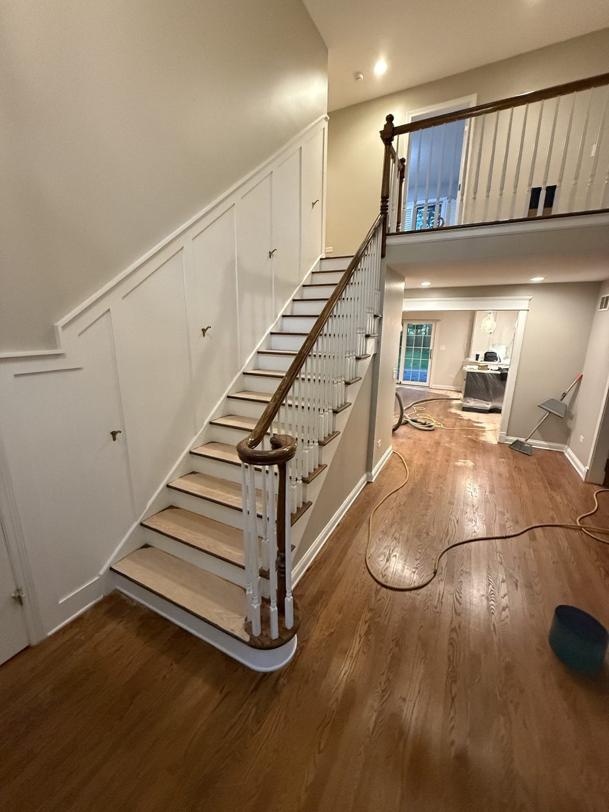 Two-story foyer with worn orange-toned red oak floors mid-refinishing, Chicago-area home