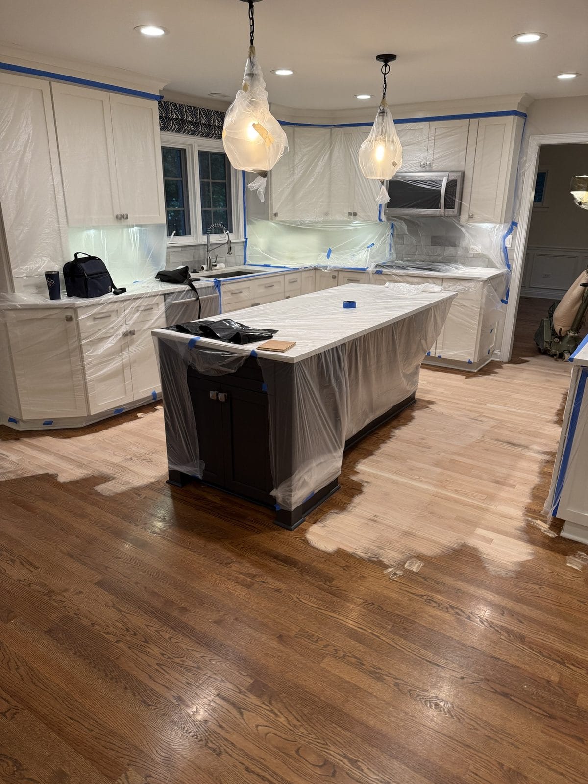 Red oak kitchen floor before refinishing in a Chicago-area home, cabinets masked off for dust control